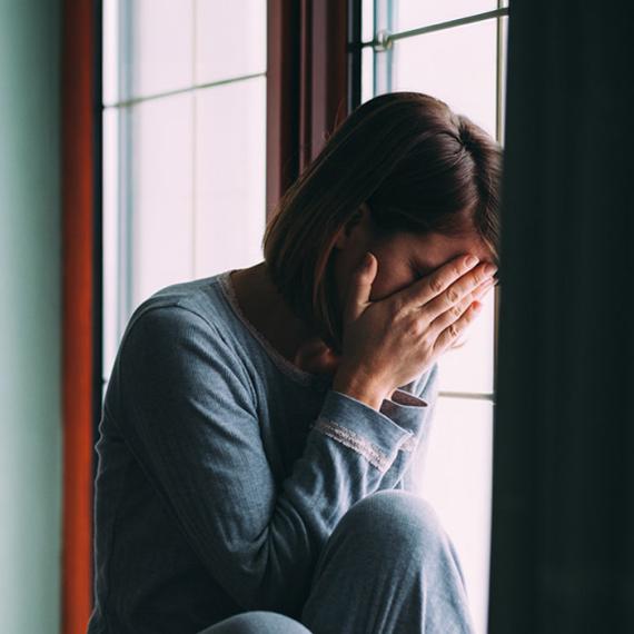 Woman in windowsill with hand covering face in despair 